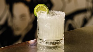 A glass of a clear beverage with a lime slice garnish, placed on a reflective surface with a blurred background. - Bar Broadway (Chippendale)