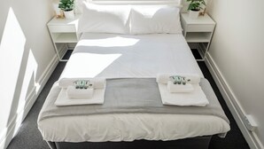 A neatly made bed with white linens and towels, a grey blanket, and a window with a view of buildings. - Bar Broadway (Chippendale)