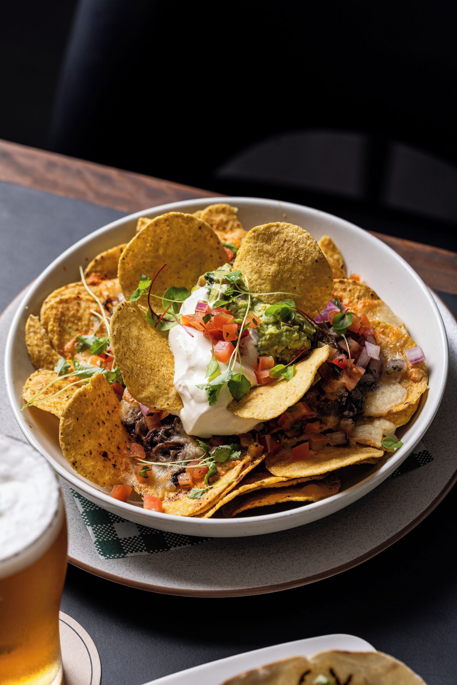 Un plato de nachos cubiertos con crema agria, guacamole y tomates picados.