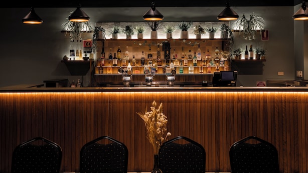 A bar area with wooden paneling, multiple hanging pendant lights, and shelves stocked with bottles. - Unanderra Hotel  (Unanderra)