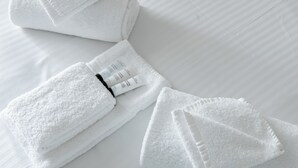 Neatly folded white towels and a bottle of lotion on a white bed. - Unanderra Hotel  (Unanderra)