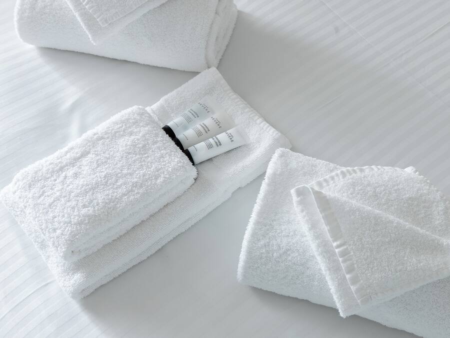 Toalhas brancas bem dobradas e um frasco de loção sobre uma cama branca.