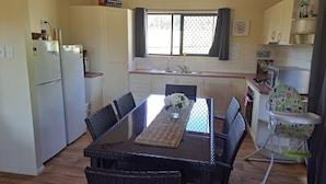 Une cuisine de taille réduite comprenant une table à manger, des chaises, un réfrigérateur, un four à micro-ondes et une fenêtre avec des rideaux.