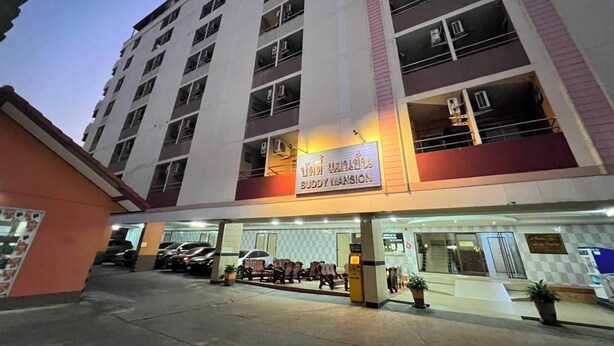 A multi-story hotel with a sign reading "BUDDY MANSION" and a parking area with several cars. - Buddy Mansion (Bangkok)
