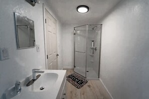 Ein Badezimmer mit weißem Waschbecken, Spiegel und Duschkabine aus Glas.