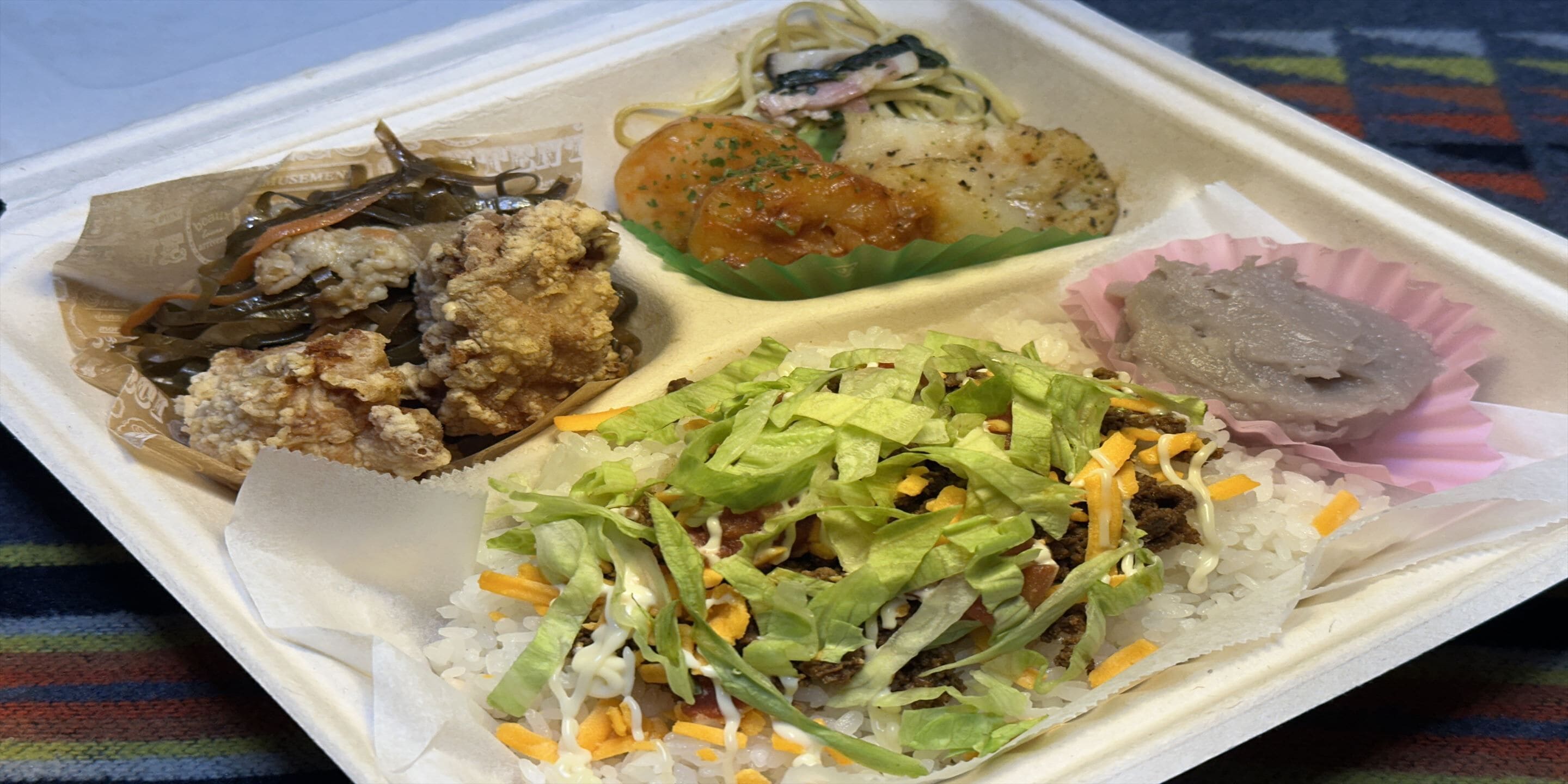 Un repas à emporter comprenant divers plats, notamment du poulet frit, des nouilles et une salade.