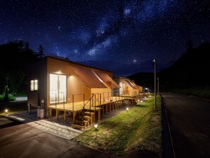A row of wooden cabins with a starry night sky above, connected by a covered walkway. - Yambaru Experience Hotel Nunganiku (Higashi)