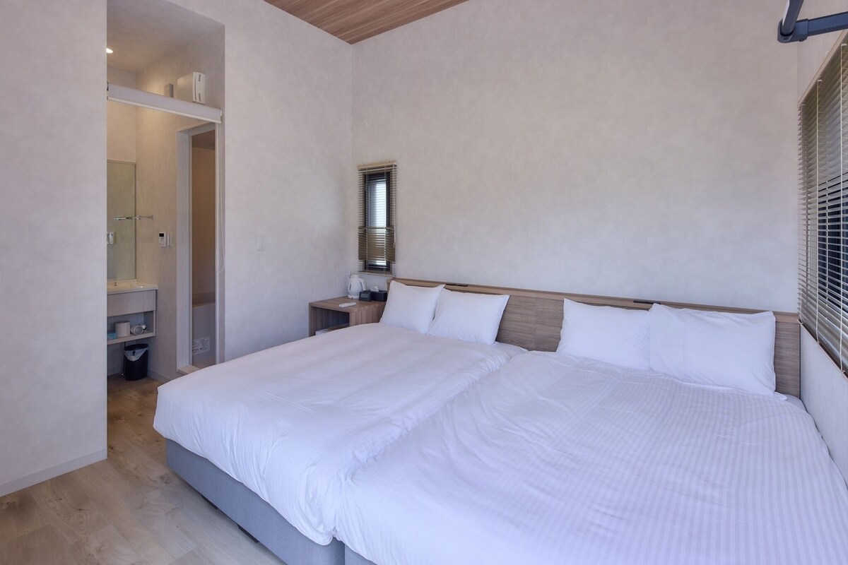 Une chambre moderne avec un grand lit, une table de chevet, un miroir et une fenêtre avec des stores.