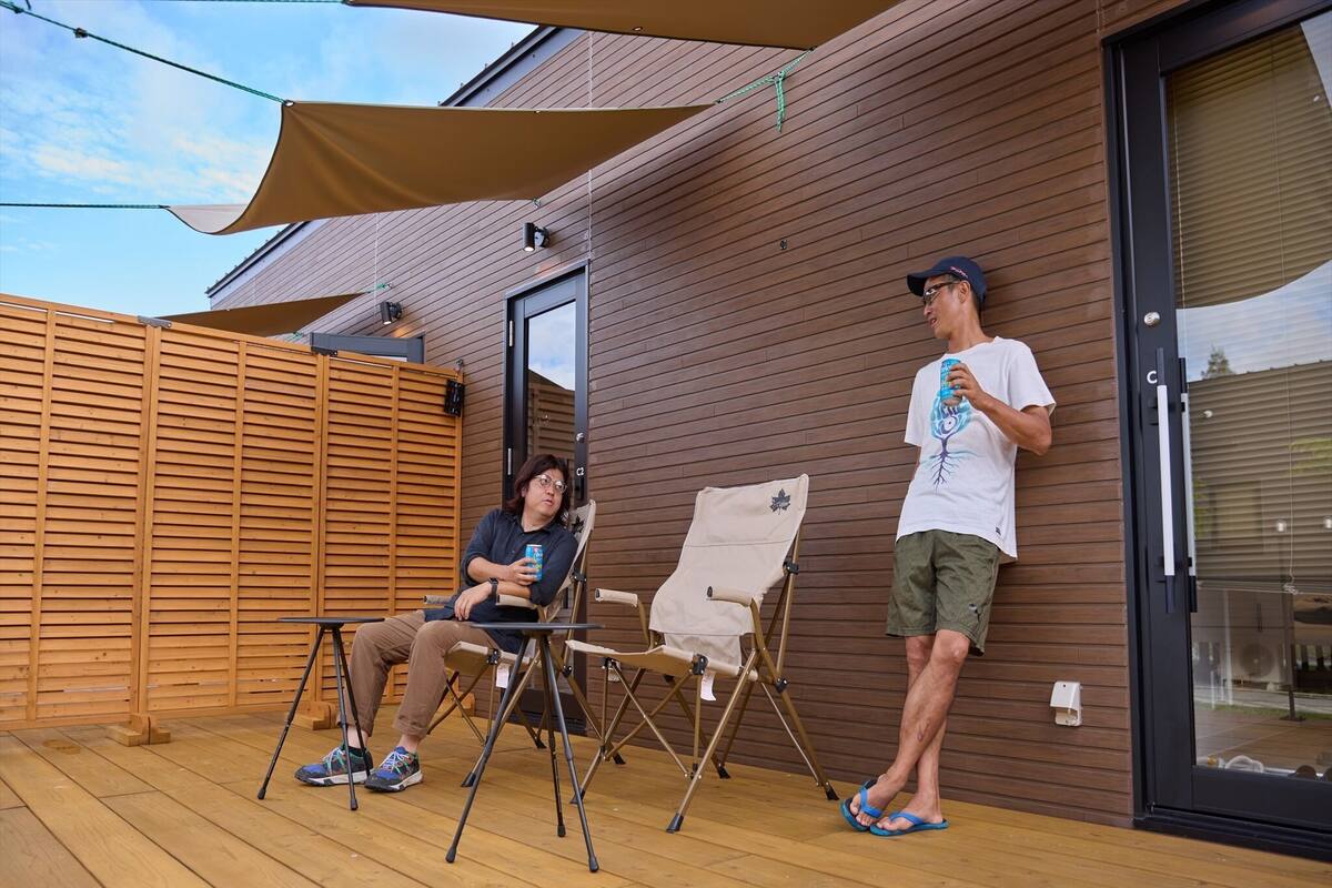 Una terrassa de fusta amb dues cadires plegables, una taula i un parasol gran que fa ombra.