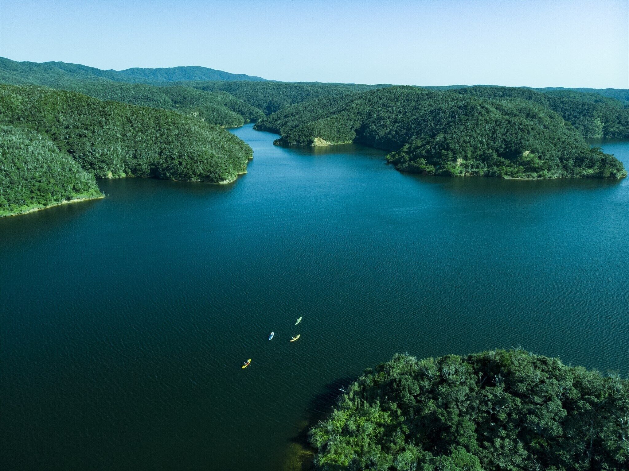 Vista aérea de una extensa masa de agua rodeada de colinas cubiertas de bosques densos.