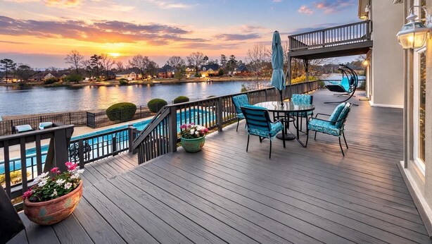 Eine Holzterrasse mit Pool, Gartenmöbeln und Blick auf einen See bei Sonnenuntergang.