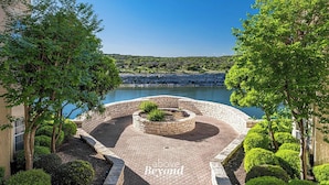 A landscaped courtyard with a circular brick feature, a view of a body of water, and a building with a tower. - Sunset & Lakeview from Castle Turret on The Island (Lago Vista)