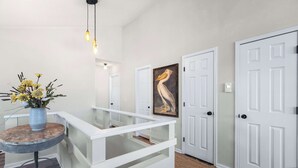 Un corridoio con porte bianche, un parapetto in vetro, un vaso con fiori gialli e un quadro di un pellicano.