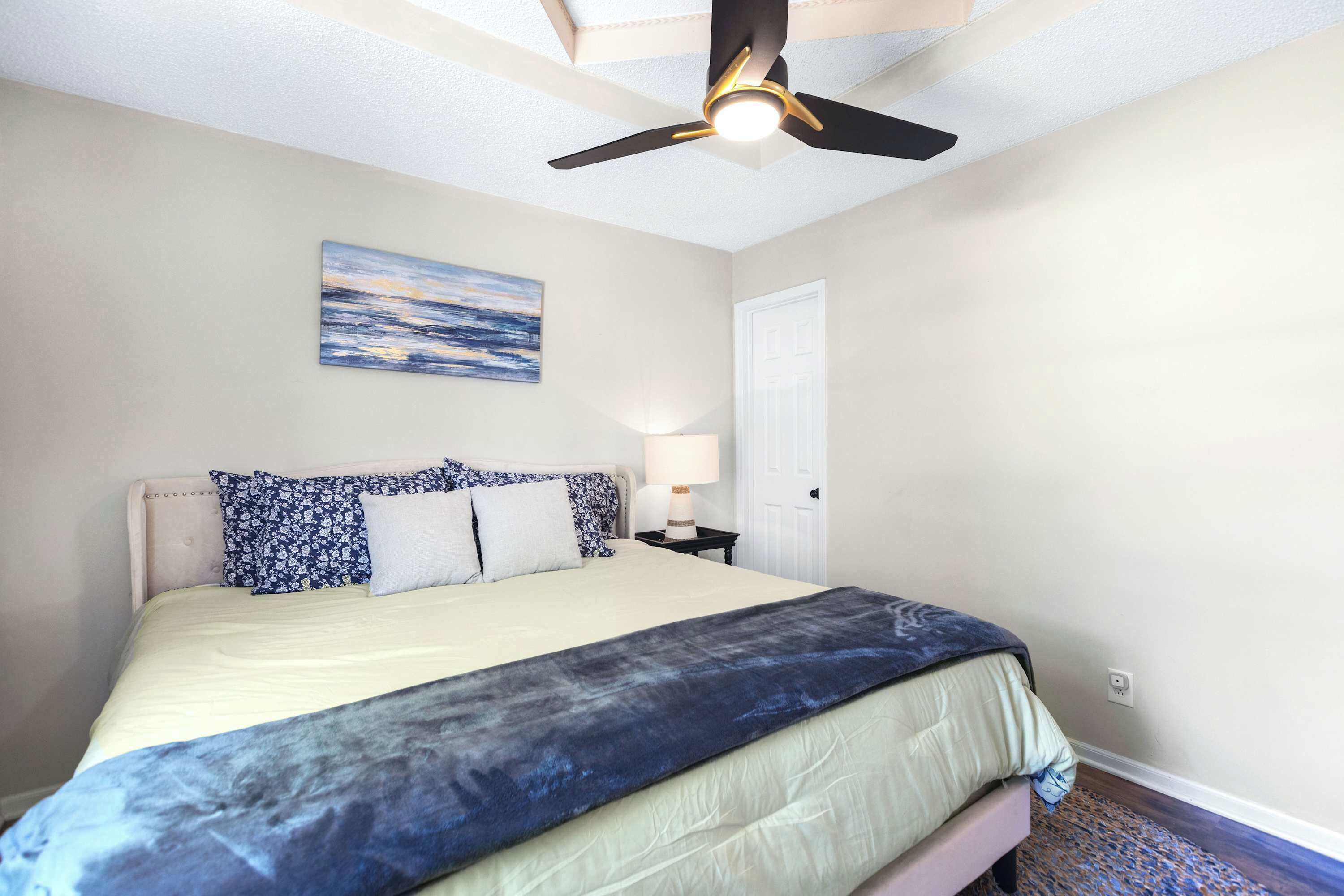 A bedroom with a bed, a ceiling fan, a nightstand, a lamp, and a door.