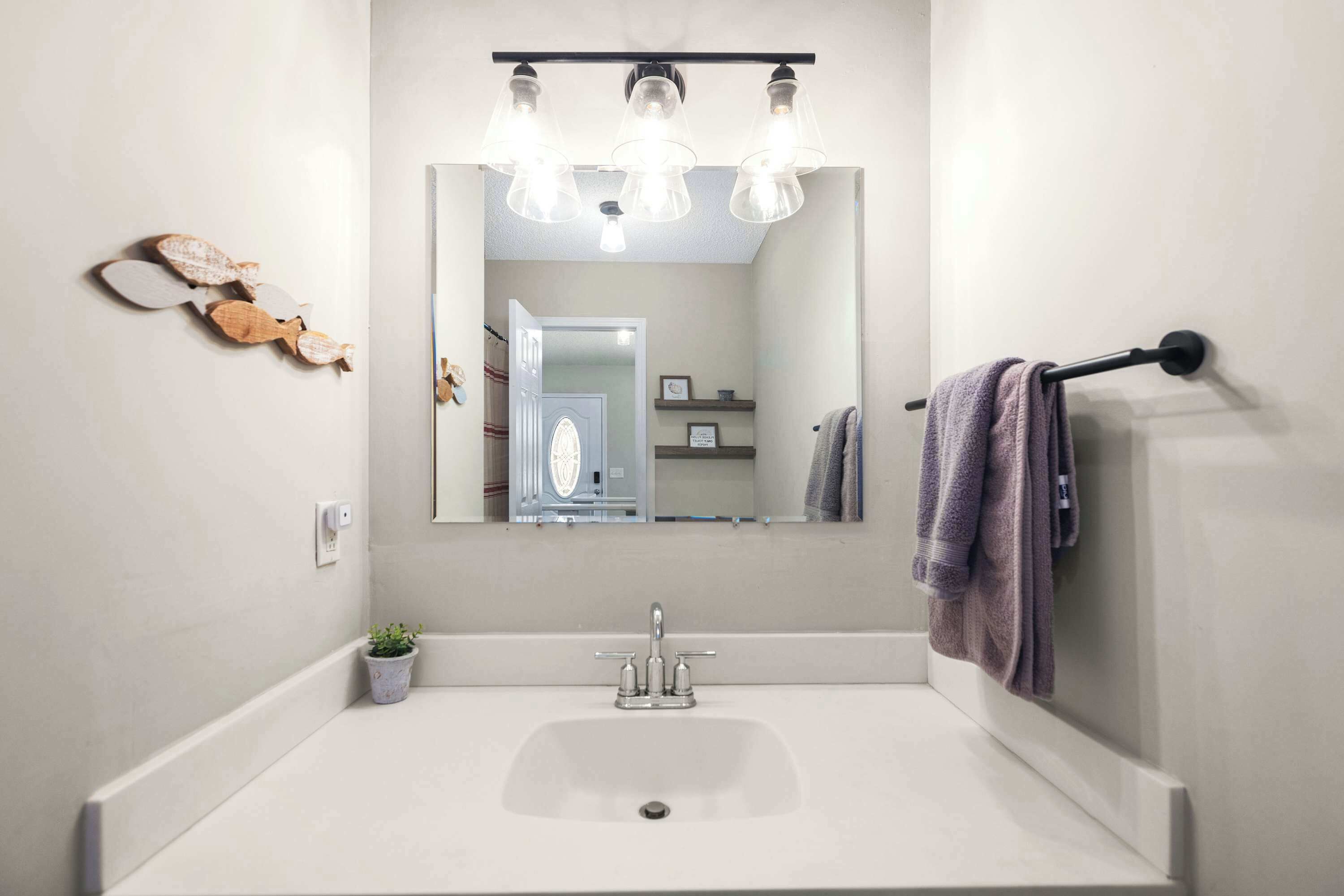 Un baño con un lavabo blanco, un espejo y tres lámparas colgantes.