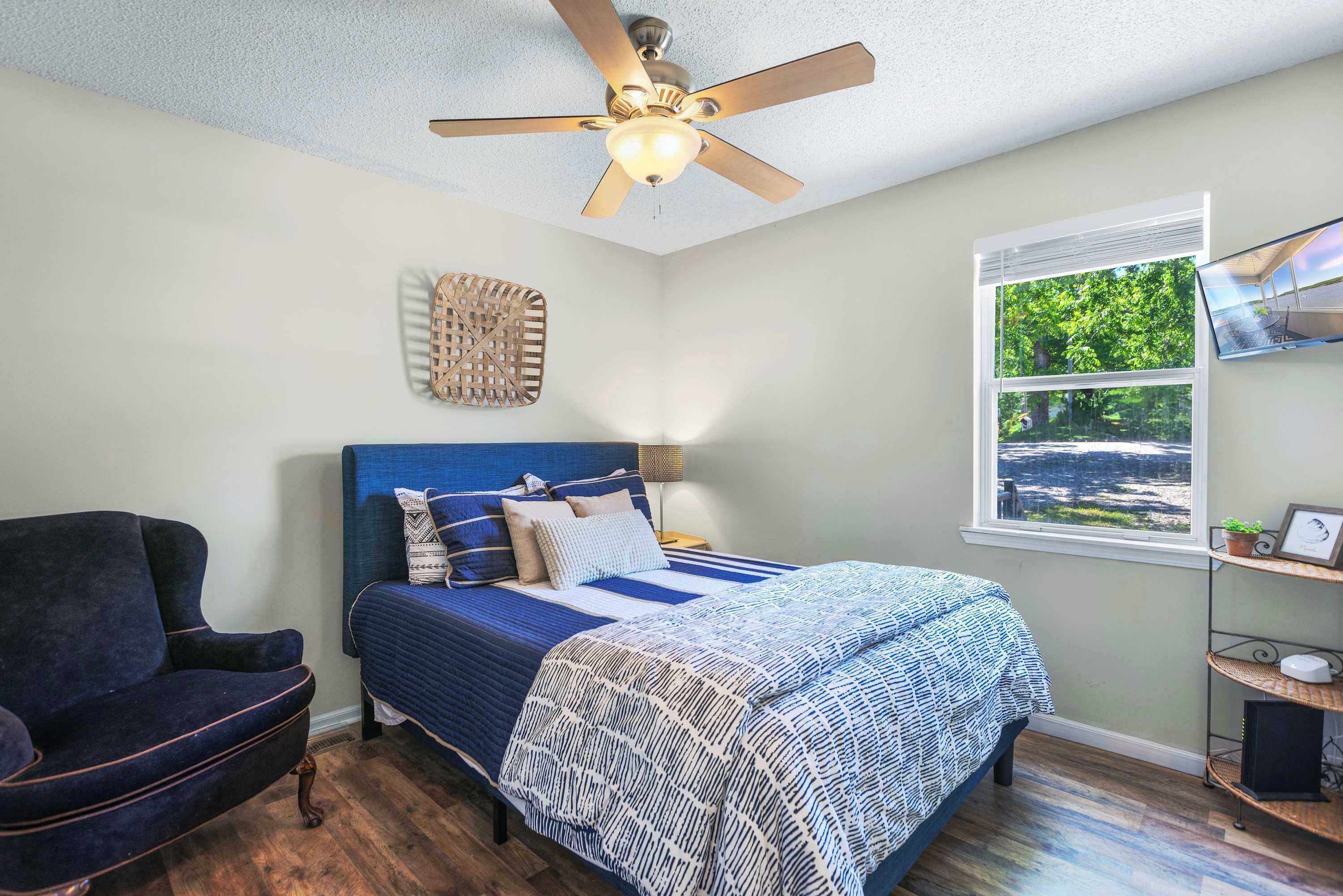 A bedroom with a bed, a chair, a ceiling fan, a window with blinds, and a shelf with items.