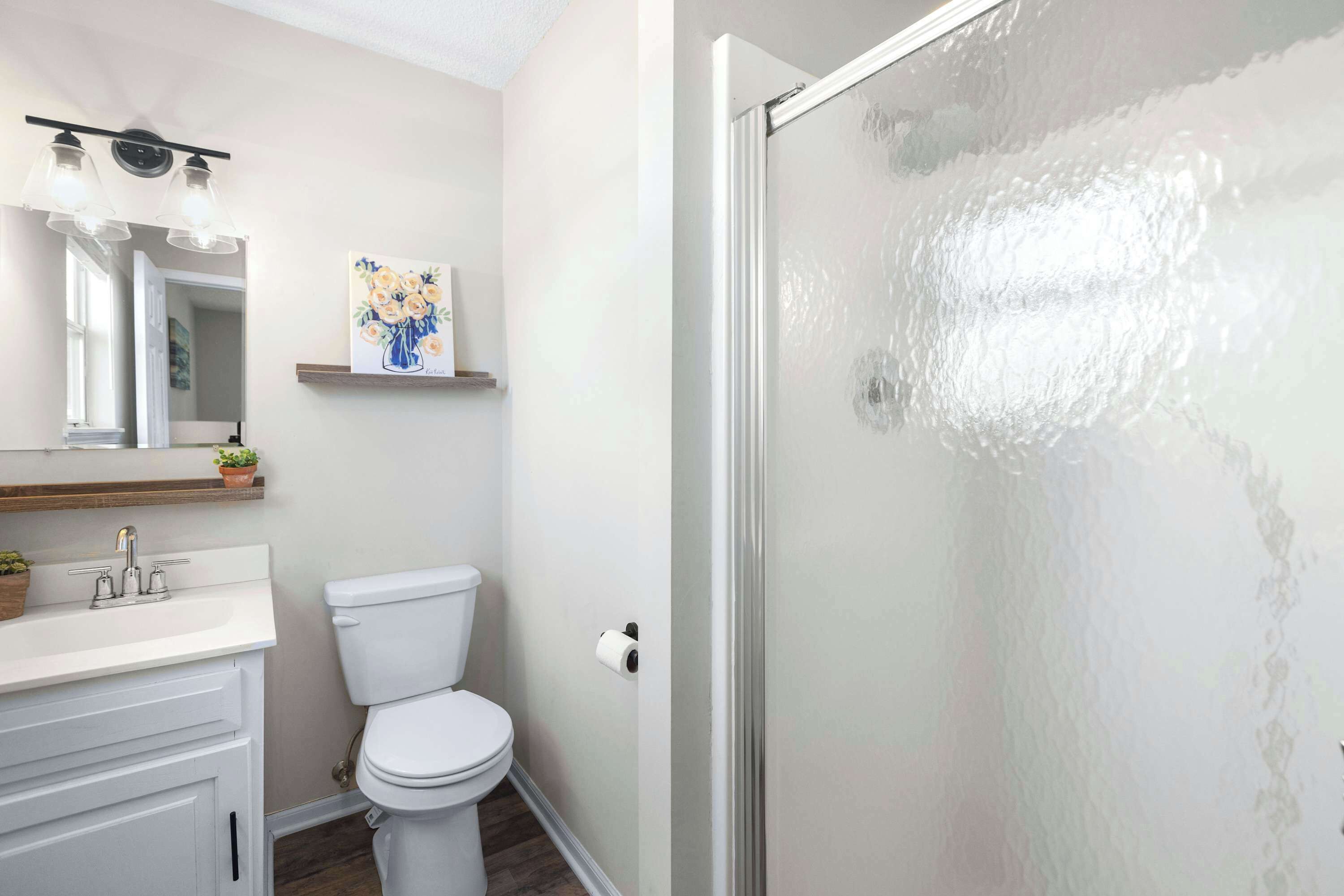 Un bagno con lavandino bianco, un water, uno specchio e una doccia con porta in vetro satinato.
