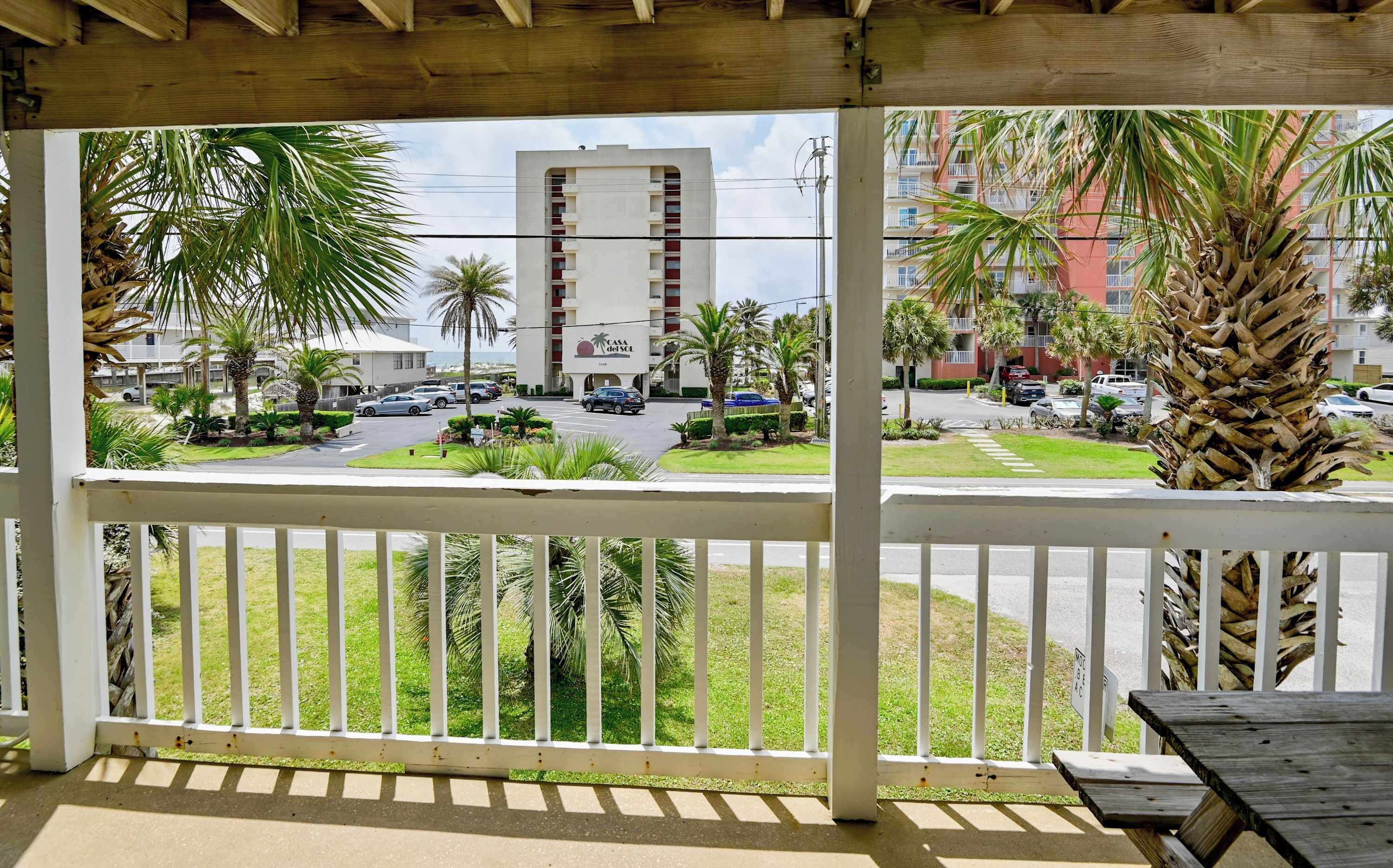 Une vue depuis un balcon doté d’une balustrade en bois, donnant sur une rue où sont garées des voitures et sur un immeuble avec des balcons.