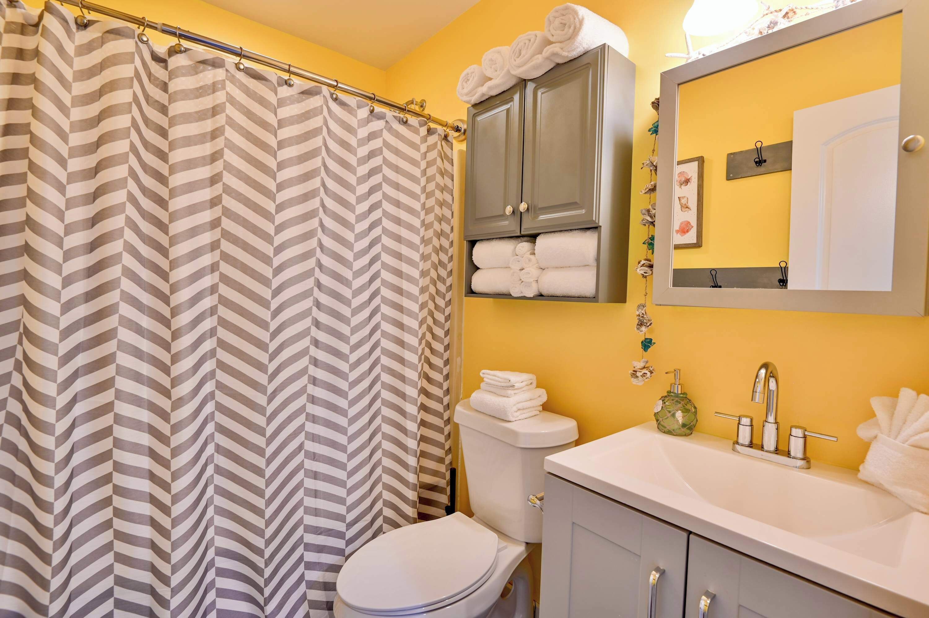 A bathroom with a striped shower curtain, a toilet, a sink with a mirror, and a cabinet with towels.