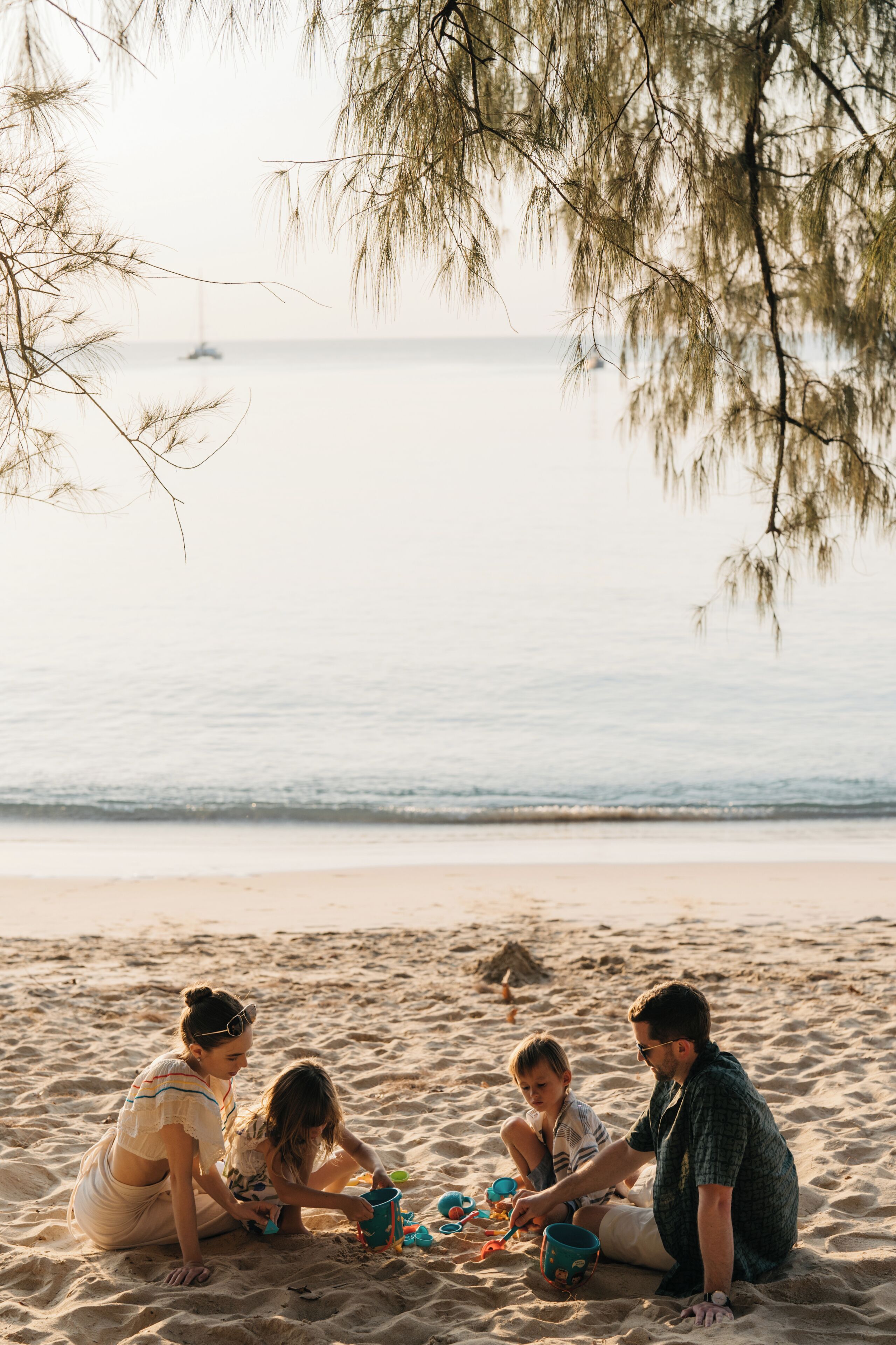 Una familia de cuatro personas en una playa arenosa, con un mar tranquilo y un barco a lo lejos.