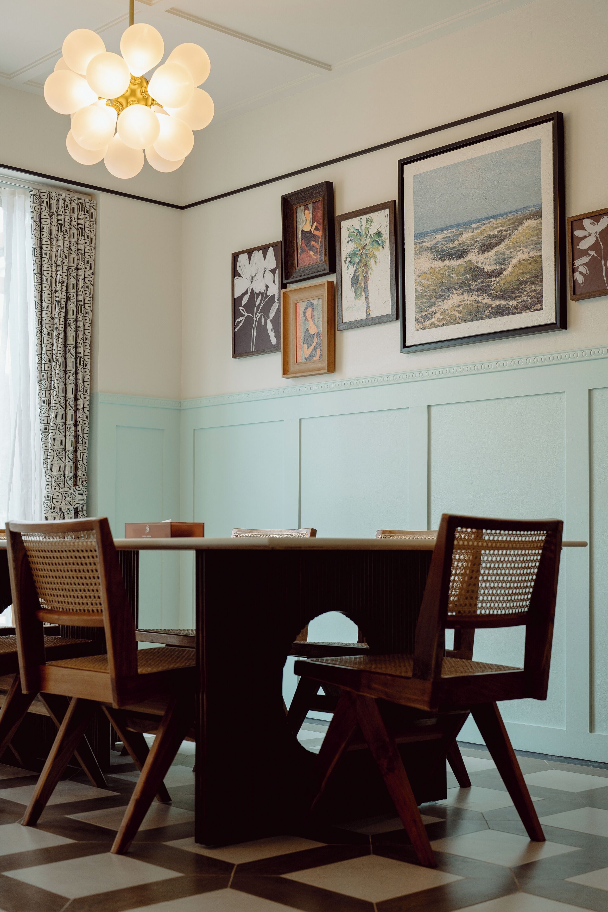 Un comedor con una mesa y sillas, una obra de arte enmarcada en la pared y una cortina estampada.