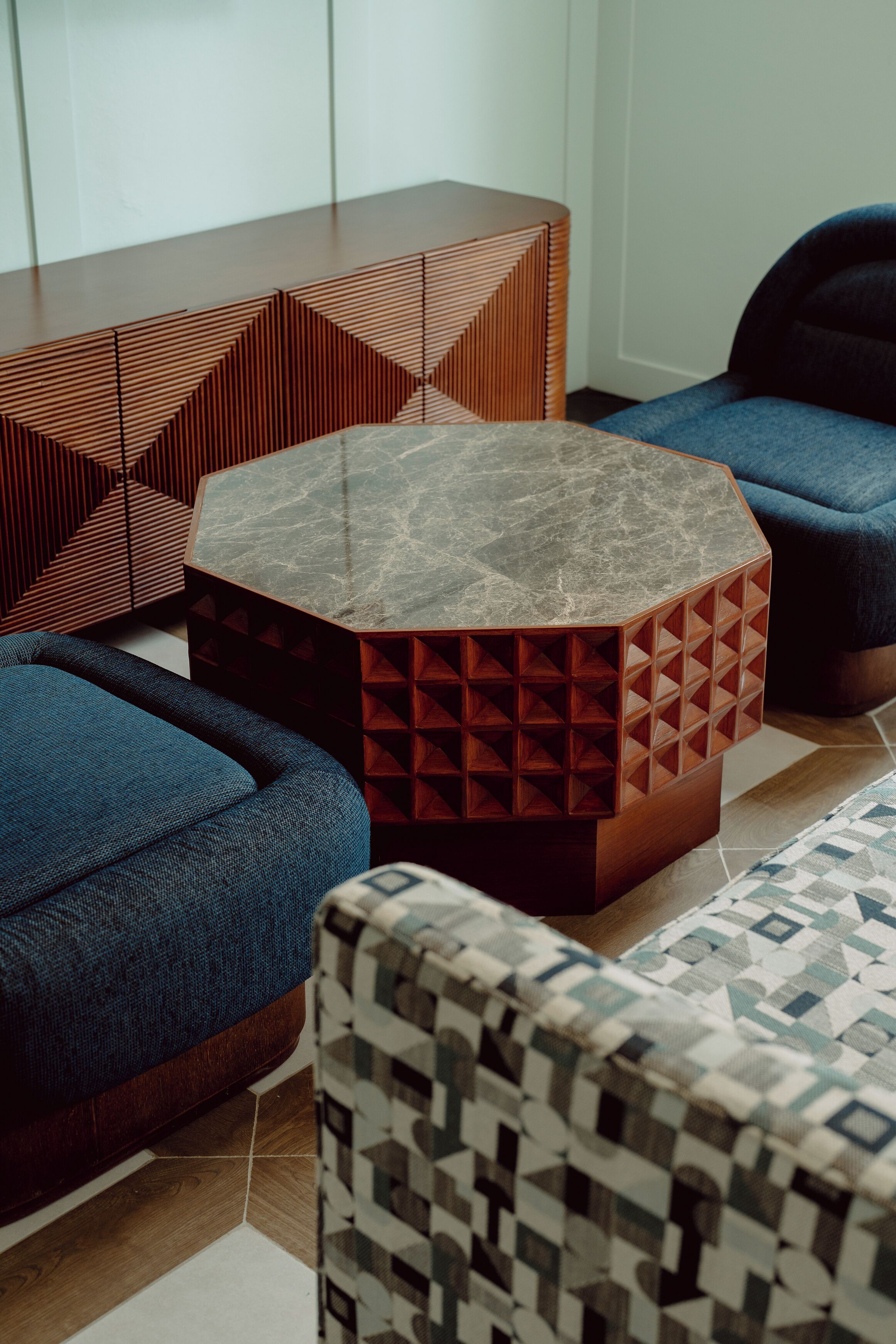 A modern living room with a geometric coffee table, blue sofas, and patterned cushions.