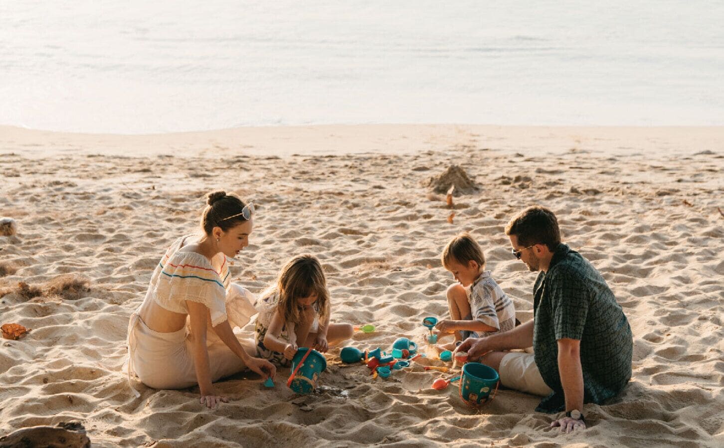 Une famille de quatre personnes sur une plage de sable, sous un ciel dégagé.