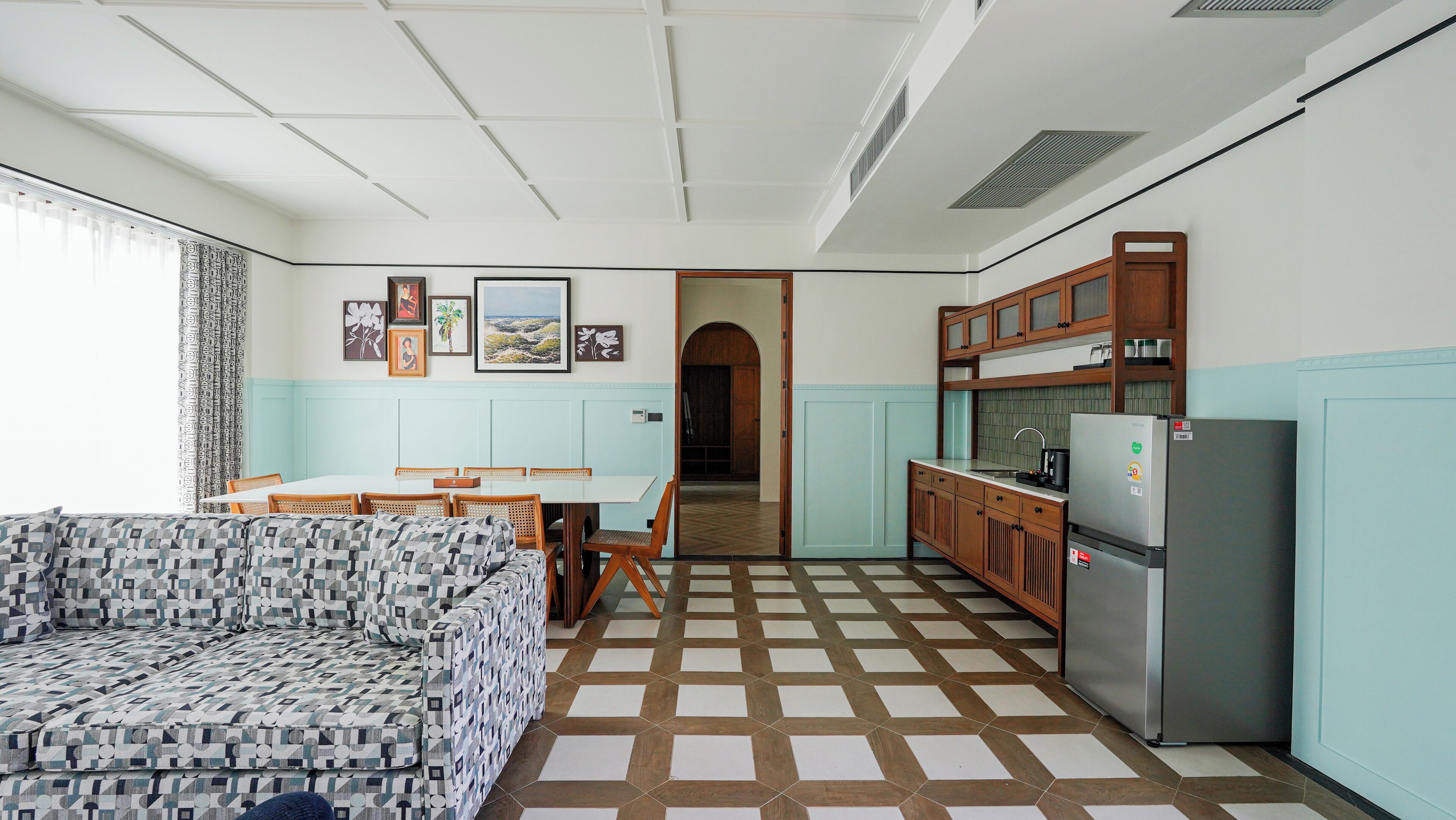 Una cocina compacta con zona de comedor, un sofá estampado y un refrigerador.
