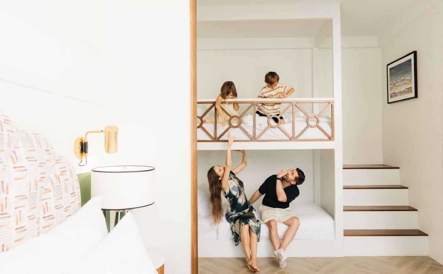 A room with a bunk bed, a lamp, a staircase, and a framed picture on the wall.