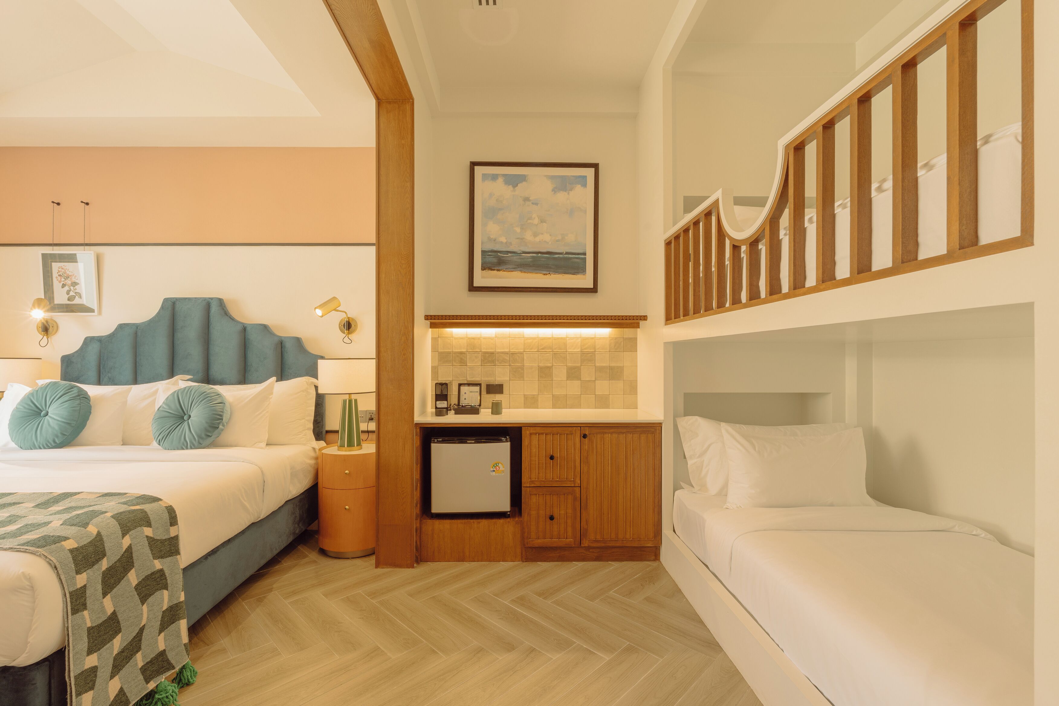 A hotel room with a bed, a small kitchenette, a wooden staircase, and a painting on the wall.
