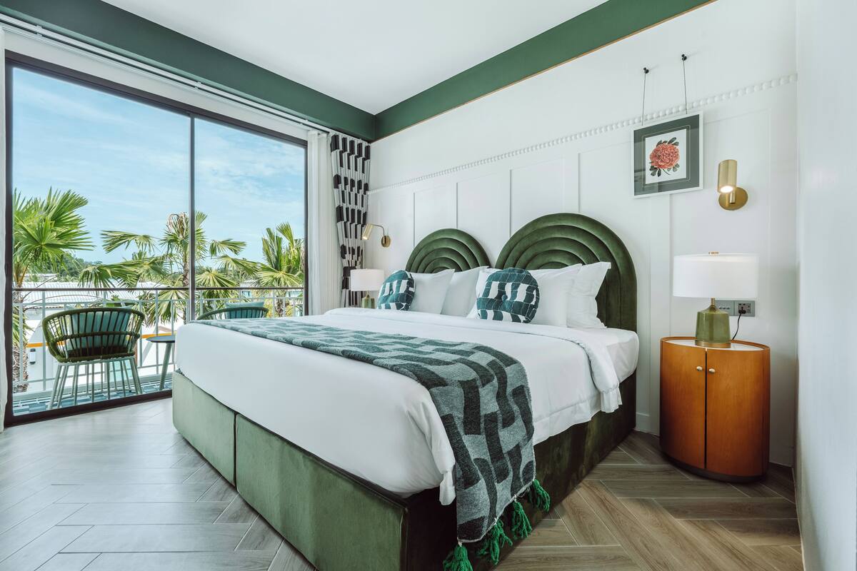 Une chambre d’hôtel moderne avec un grand lit, une table de chevet, une chaise et une vue sur des palmiers.