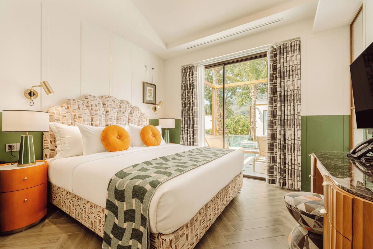 Une chambre d’hôtel dotée d’un grand lit, d’un bureau avec un téléviseur à écran plat, d’une table de chevet et offrant une vue sur l’extérieur grâce à une porte-fenêtre coulissante.