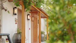 Une pergola en bois avec une porte coulissante, un luminaire fixé au mur et des plantes en pot.