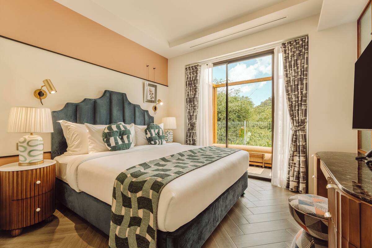 Une chambre moderne avec un grand lit, une table de chevet avec une lampe, un bureau avec une chaise et une grande fenêtre avec des rideaux.