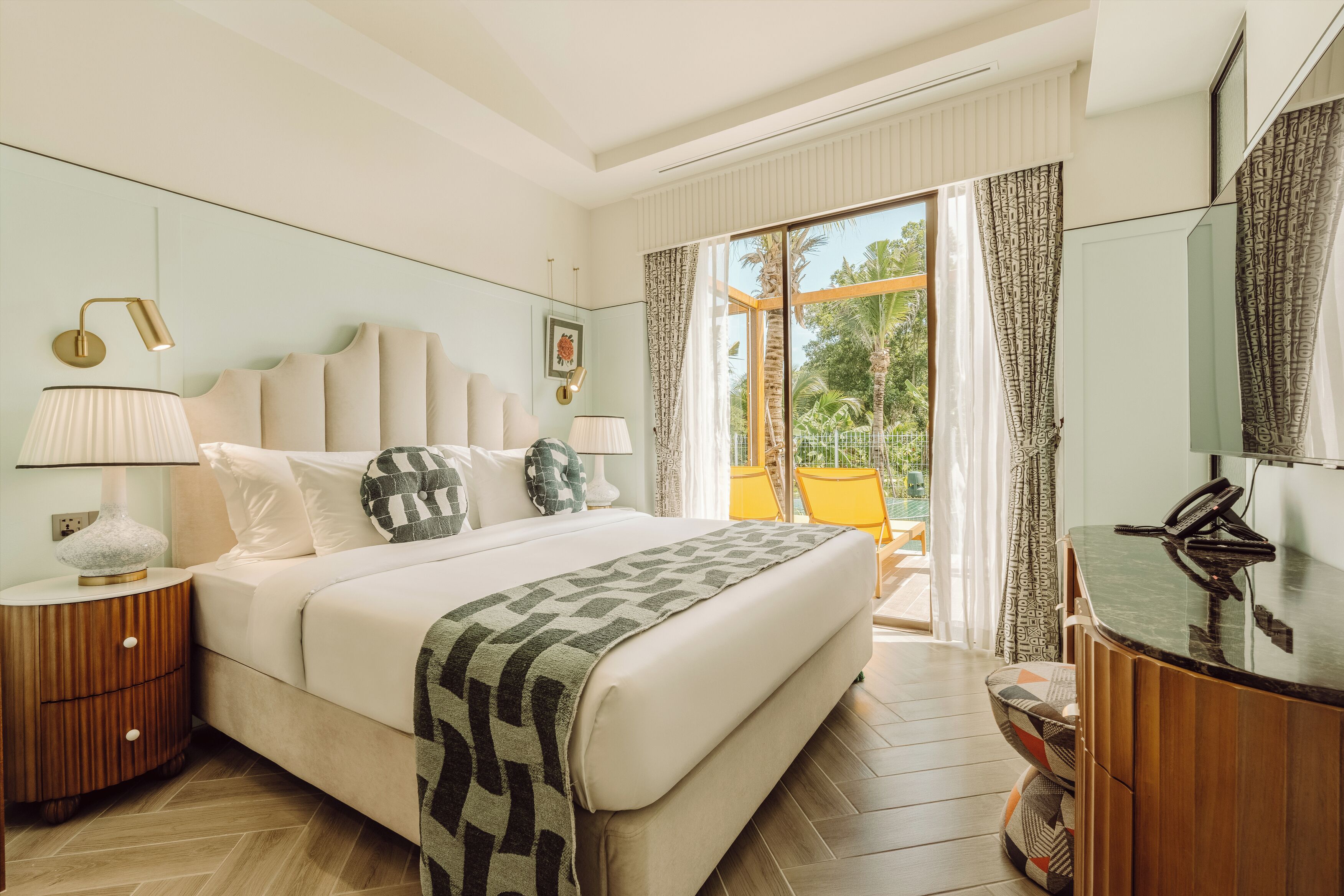 A hotel room with a large bed, two bedside tables, a desk with a telephone, and a view of the outdoors.