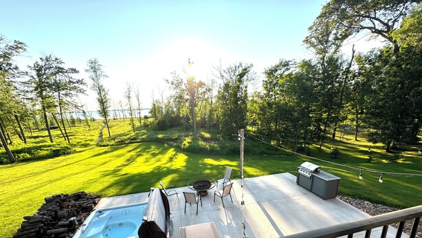 A backyard with a hot tub, barbecue grill, and outdoor seating area overlooking a well-manicured lawn and trees.