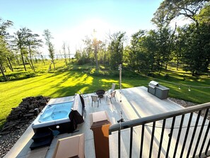 A backyard with a hot tub, barbecue grill, and outdoor seating area overlooking a well-manicured lawn and trees. - NEW - The Boardwalk on North Long Lake Brainerd with Hot Tub, Pet-Friendly (Brainerd)