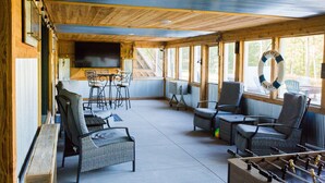 A covered outdoor seating area with wicker furniture, a foosball table, and a TV screen.