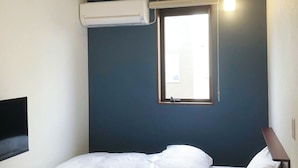 A single bed with white bedding, a small bedside table, a window with a view, and an air conditioning unit mounted on the wall. - QUEENDOM KARATSU HOTEL (Karatsu)