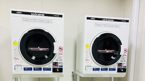 Two stacked coin-operated dryers with instructions in a foreign language, a basket, and a laundry basket. - QUEENDOM KARATSU HOTEL (Karatsu)
