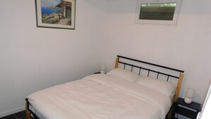A neatly made bed with white linens in a room with a small window and a framed picture on the wall. - Short-term furnished studio rental (n° 4) (Le Trait)