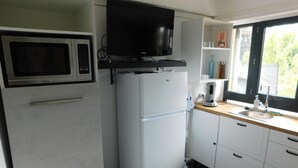 A compact kitchen with a microwave, refrigerator, and a flat-screen TV mounted above the fridge. - Short-term furnished studio rental (n° 4) (Le Trait)