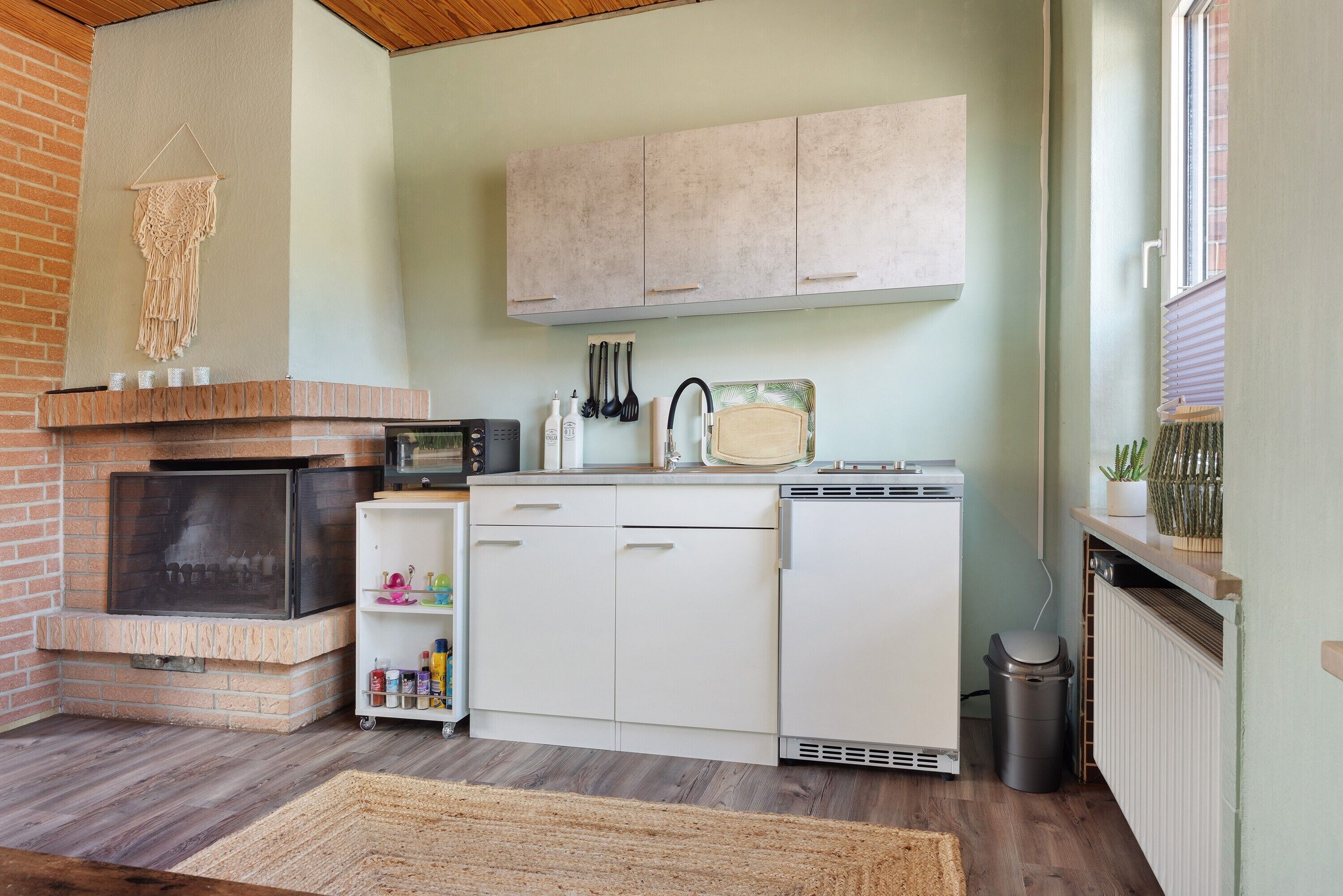 Cocina compacta con chimenea de ladrillo, armarios blancos y una pequeña isla con pileta.