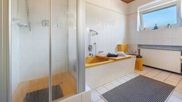 Ein Badezimmer mit Duschkabine, Holzboden, Fenster, Waschbecken und Heizkörper.