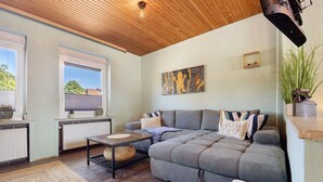 Una sala de estar con un sofá modular, una mesa, un radiador y una ventana con persianas.