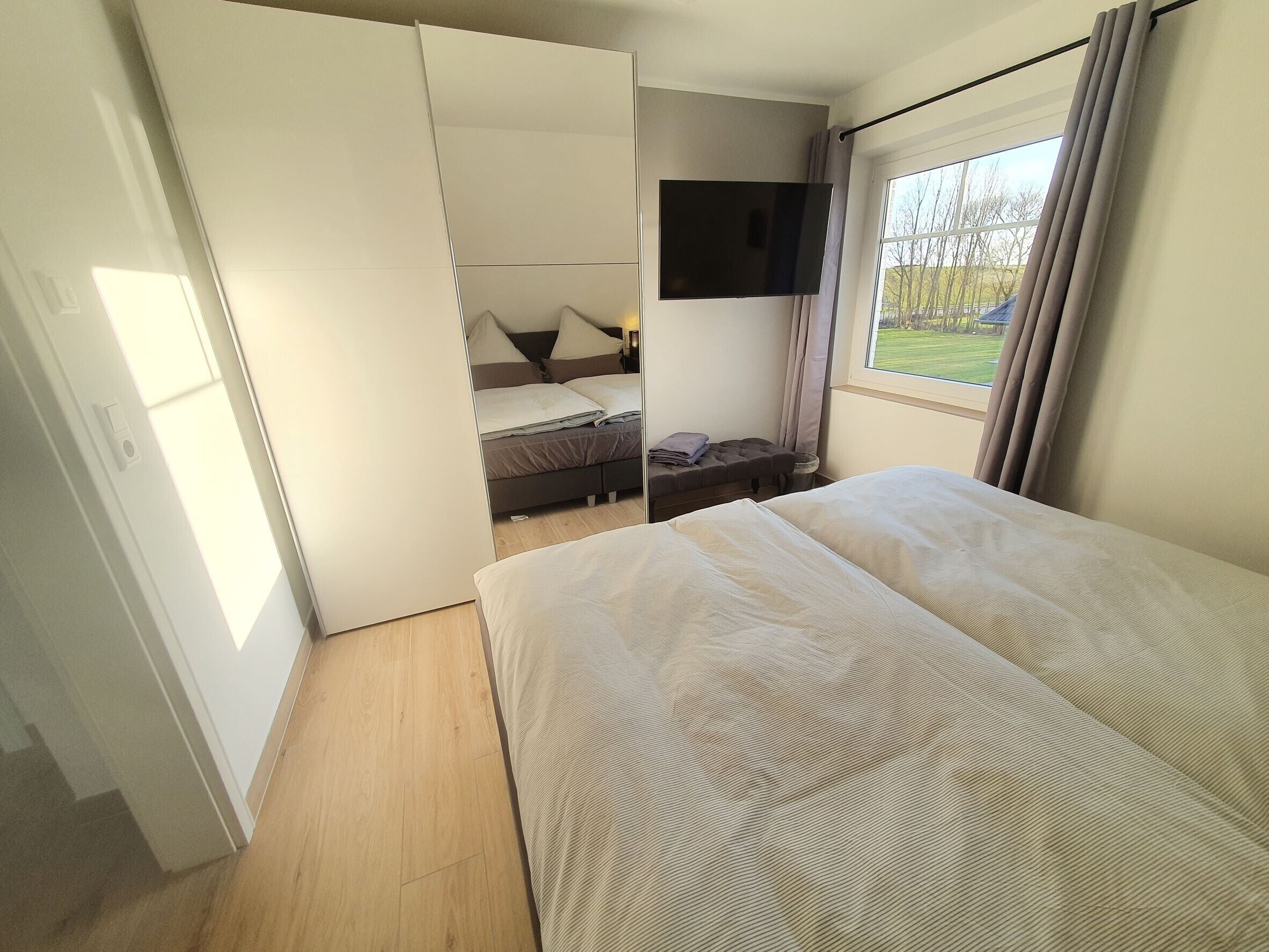 Un dormitorio con cama, televisión, ventana con cortinas y vistas al exterior.