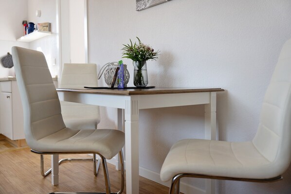 Un coin repas comprenant deux chaises blanches, une table blanche, un vase avec des fleurs et un objet décoratif posé sur la table.