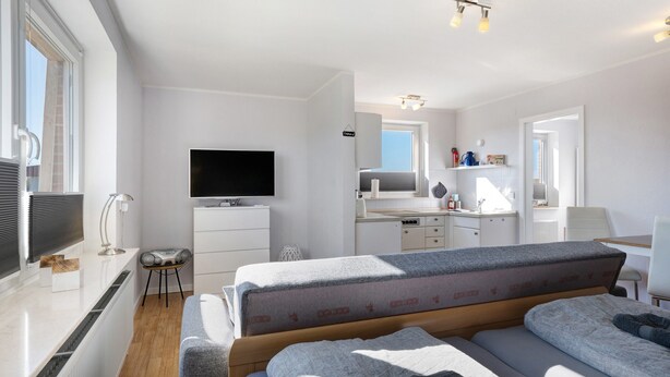 Ein modernes Hotelzimmer mit Bett, Fernseher, Schreibtisch und einer Küchenzeile.