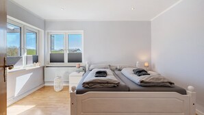 A bedroom with a bed, two bedside tables, a window, and a radiator. - Apartment 'Ferienwohnung Kapitänskajüte' with Private Terrace, Shared Garden and Wi-Fi (Nordstrand)