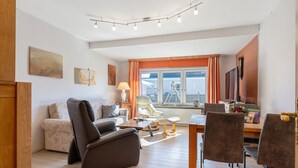 A living room with a sofa, chairs, a coffee table, and a dining table. - Apartment 'Ferienwohnung Kapitänskajüte' with Private Terrace, Shared Garden and Wi-Fi (Nordstrand)